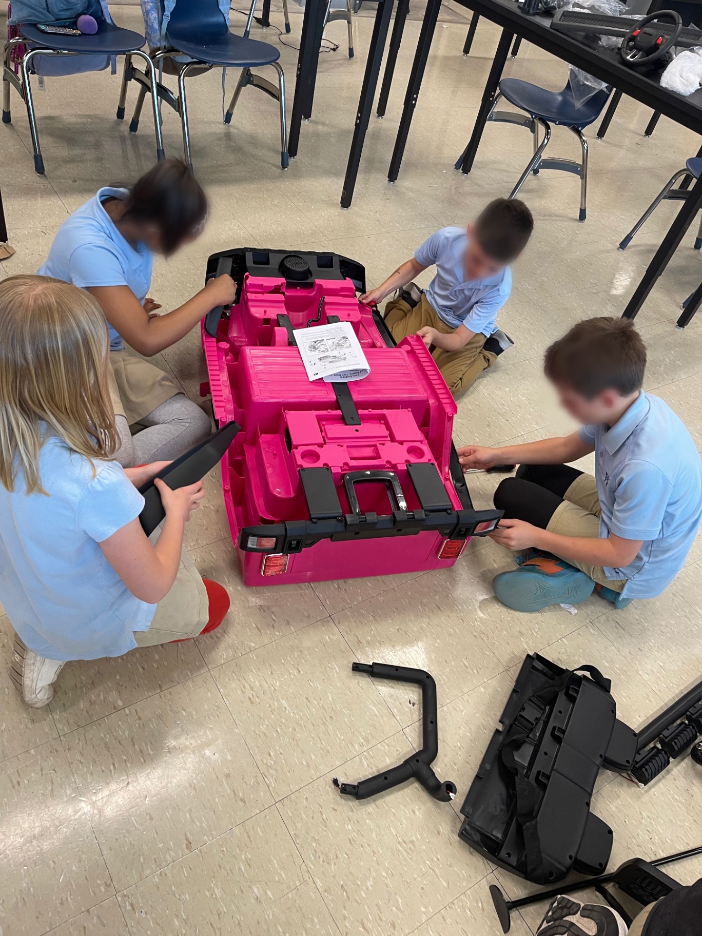 Four students carefully attaching panels to a pink adaptive ride-on car