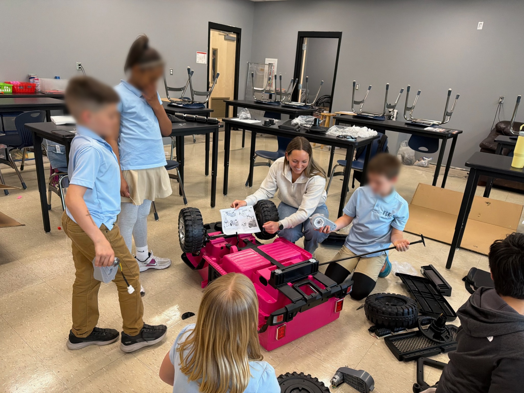 Mentor guiding students as they inspect parts of a pink ride-on car