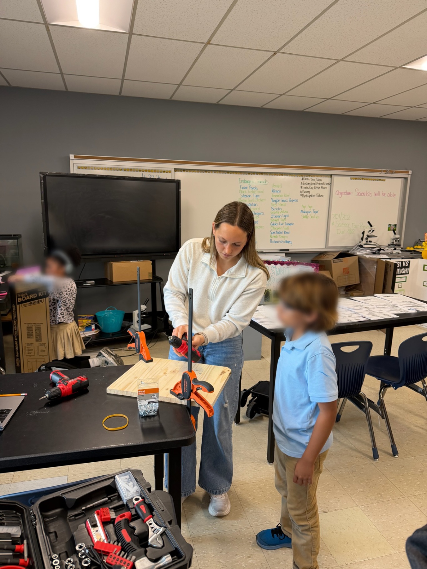 Mentor demonstrating power-drill use on wood for a young student