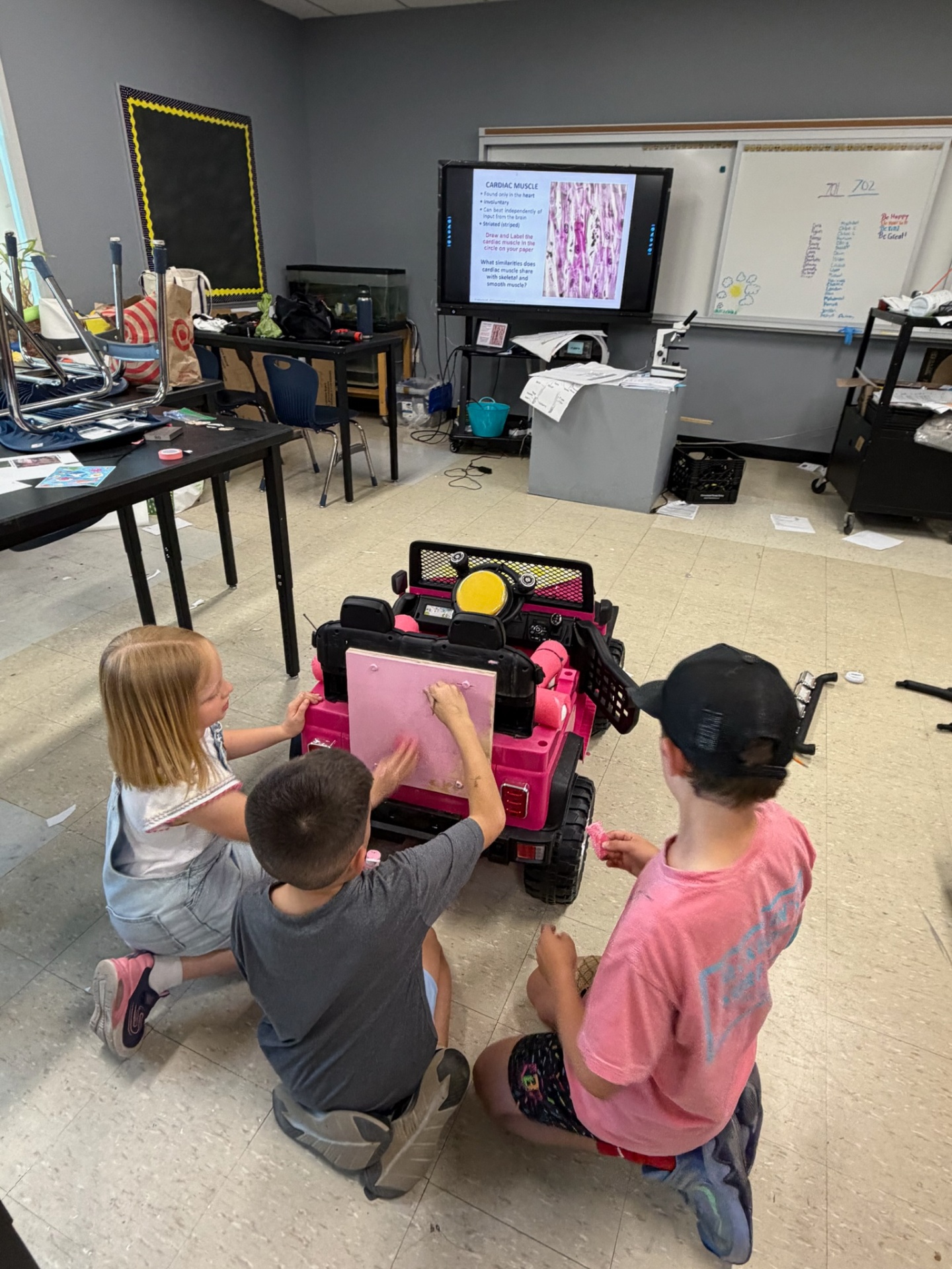 Three students adding adaptive foam supports to a pink ride-on car
