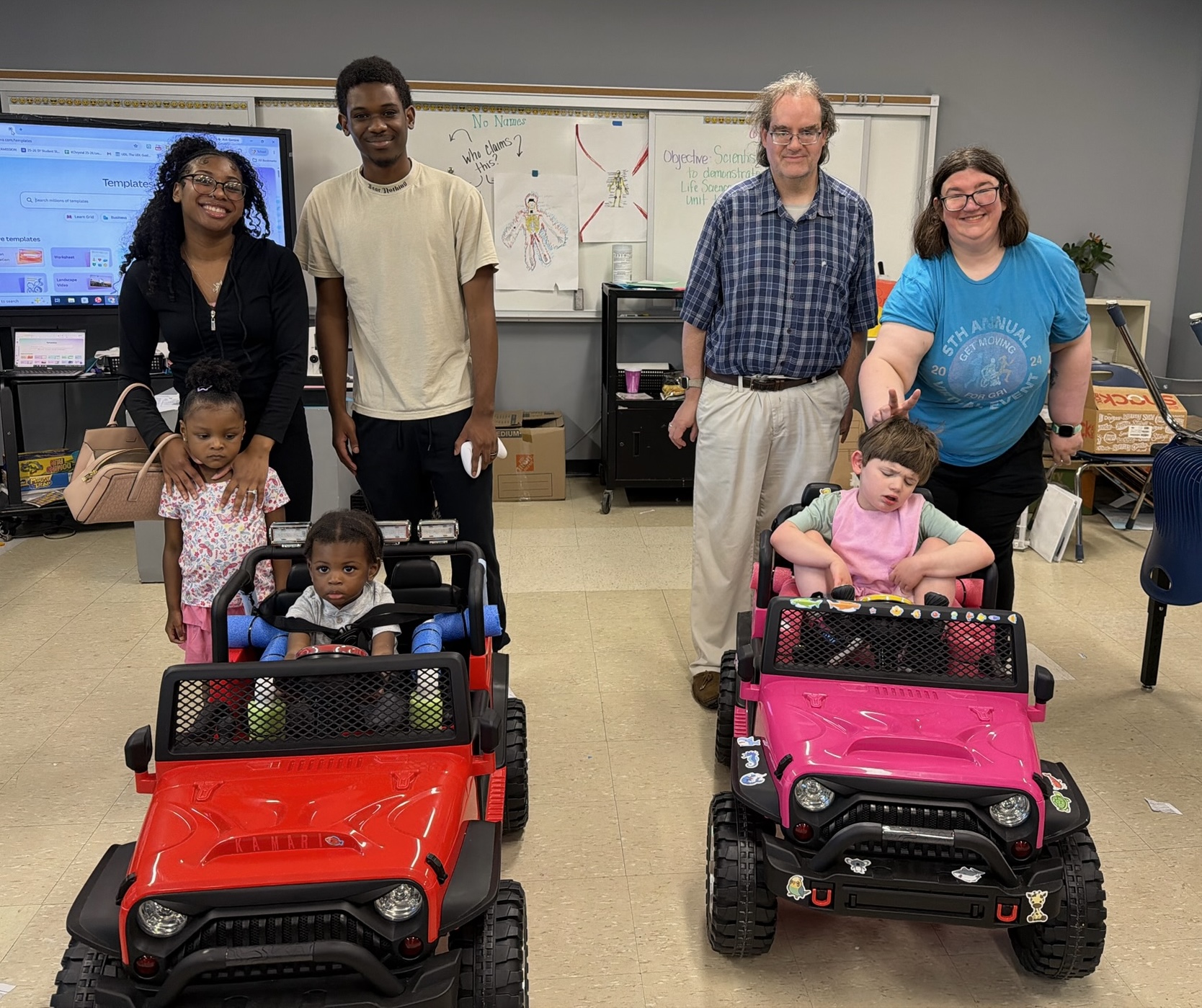 Two families with their children in newly gifted red and pink adaptive ride-on cars