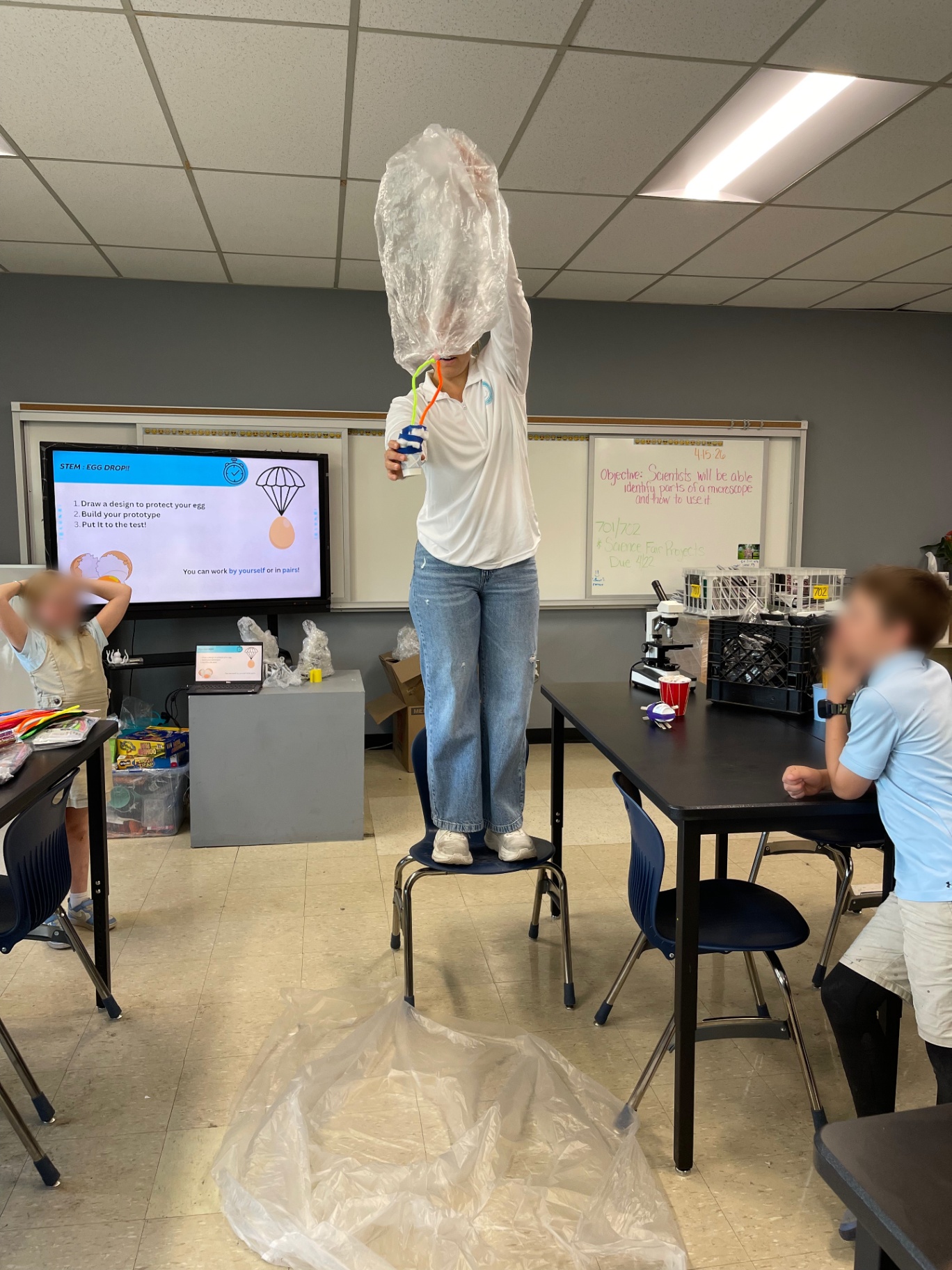Mentor standing on a chair to demonstrate an egg-drop STEM challenge