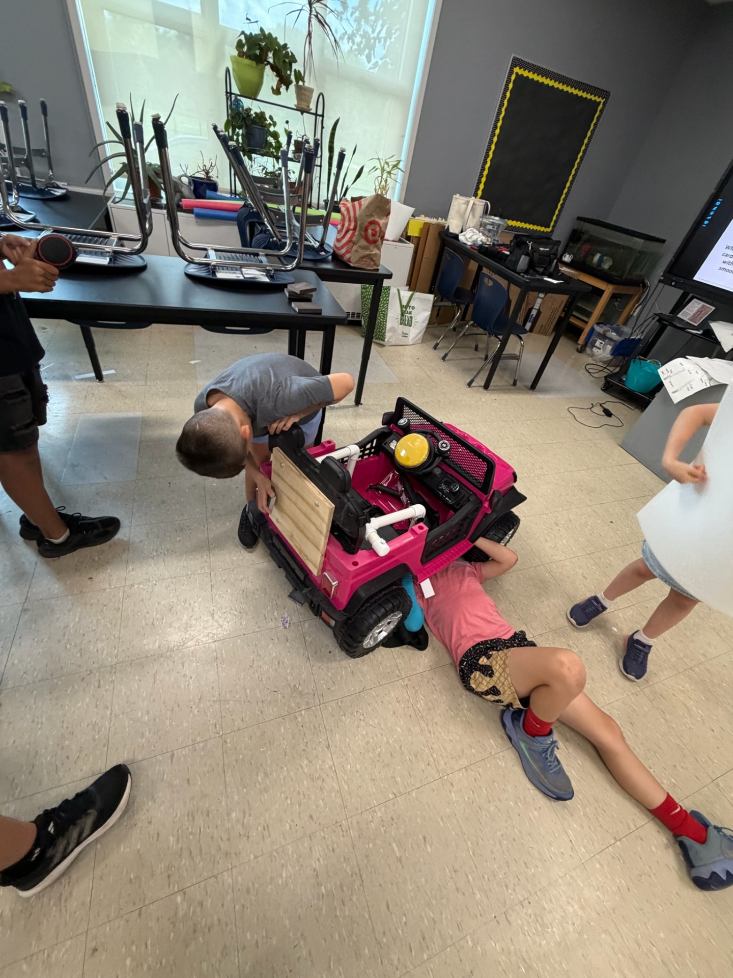 Student lying on the floor to install adaptive supports inside a pink Jeep