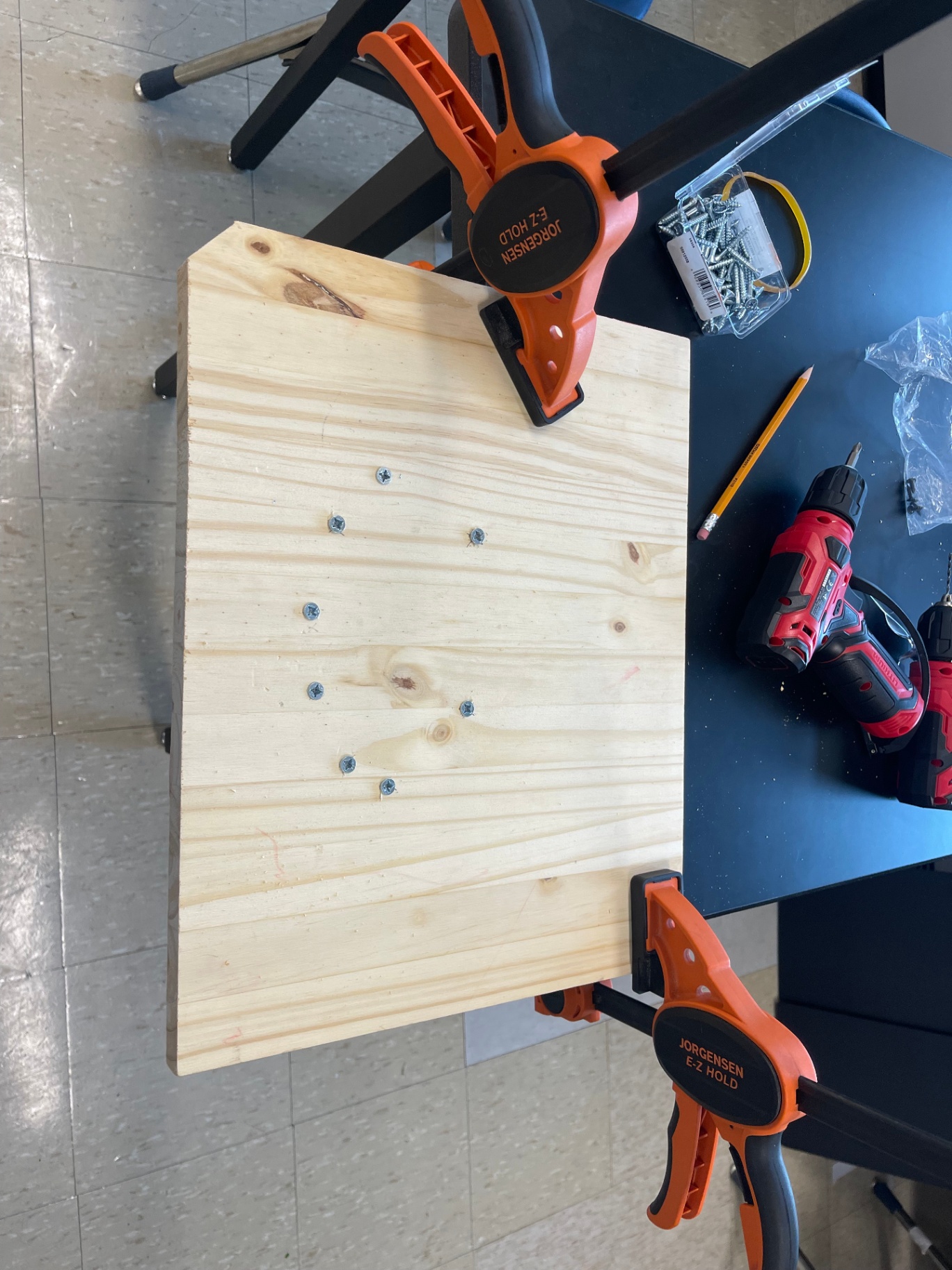 Wooden board clamped to a table with pilot holes drilled for a build project
