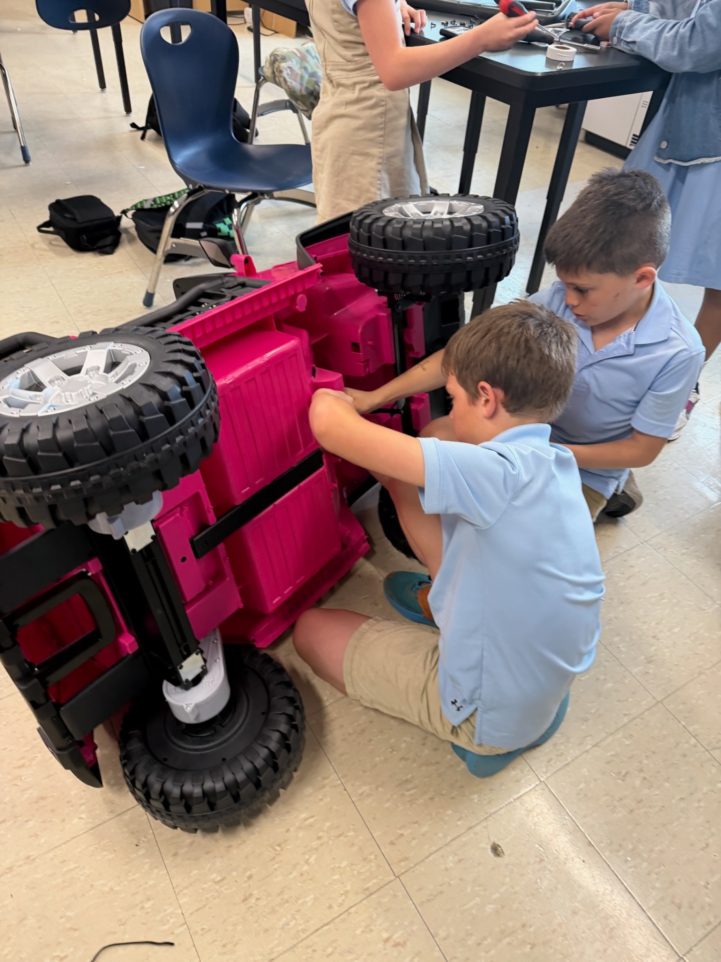 Two young students assembling wheels on an upside-down pink ride-on car