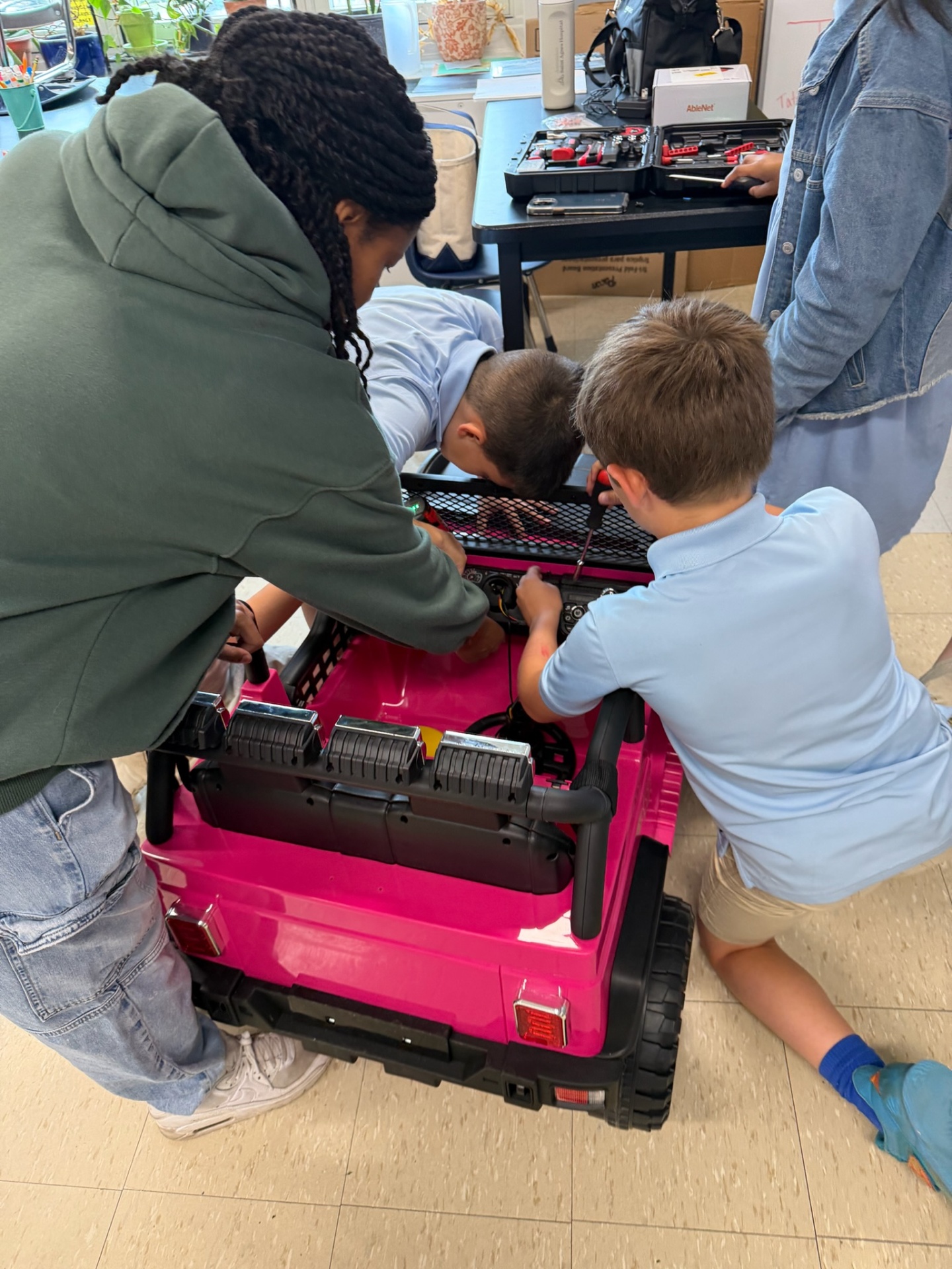 Students working together to wire the dashboard of a pink adaptive car