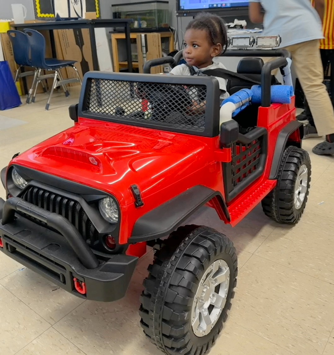 A young child smiling from the seat of a finished red adaptive Jeep
