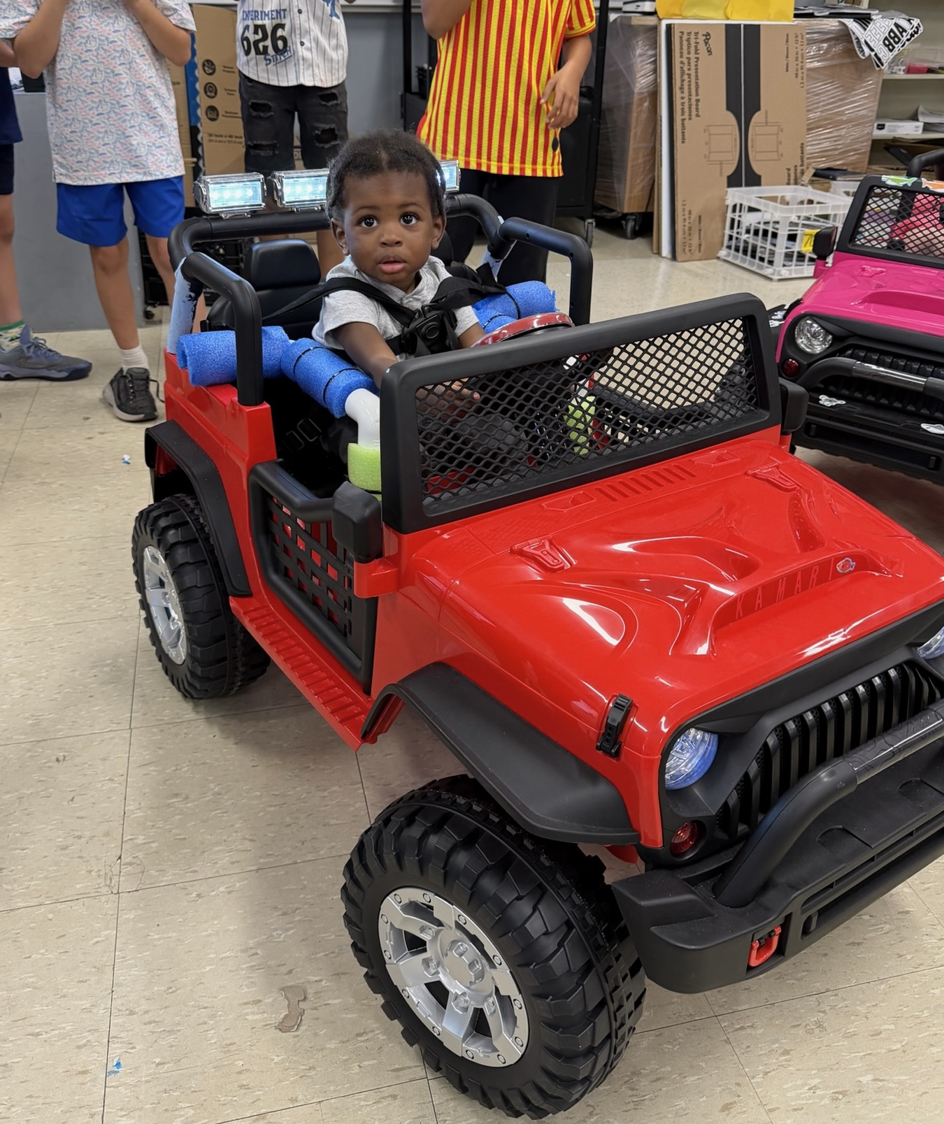 A young child smiling from the seat of a completed red adaptive Jeep