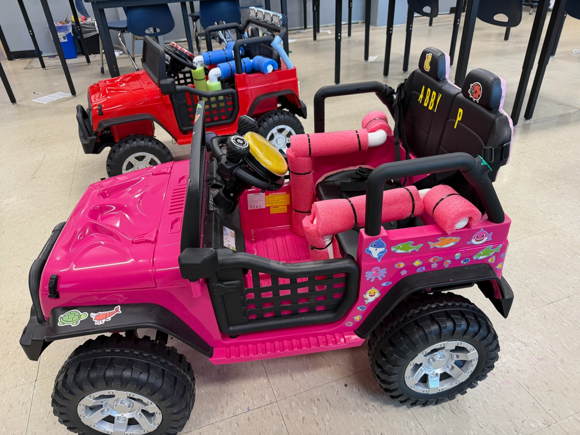 Finished pink and red adaptive ride-on cars parked side by side in the classroom