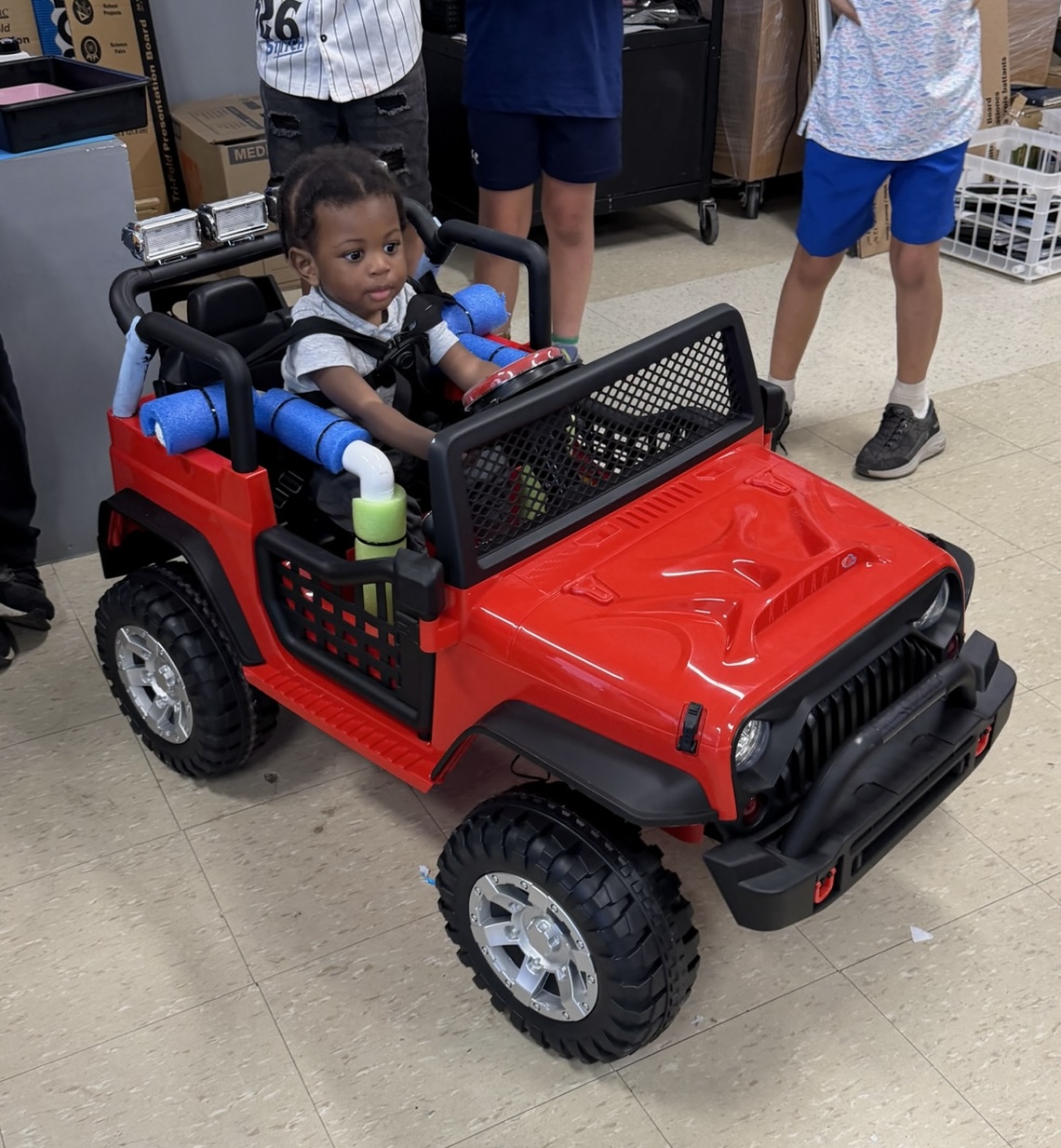A young child buckled safely into a finished red adaptive Jeep