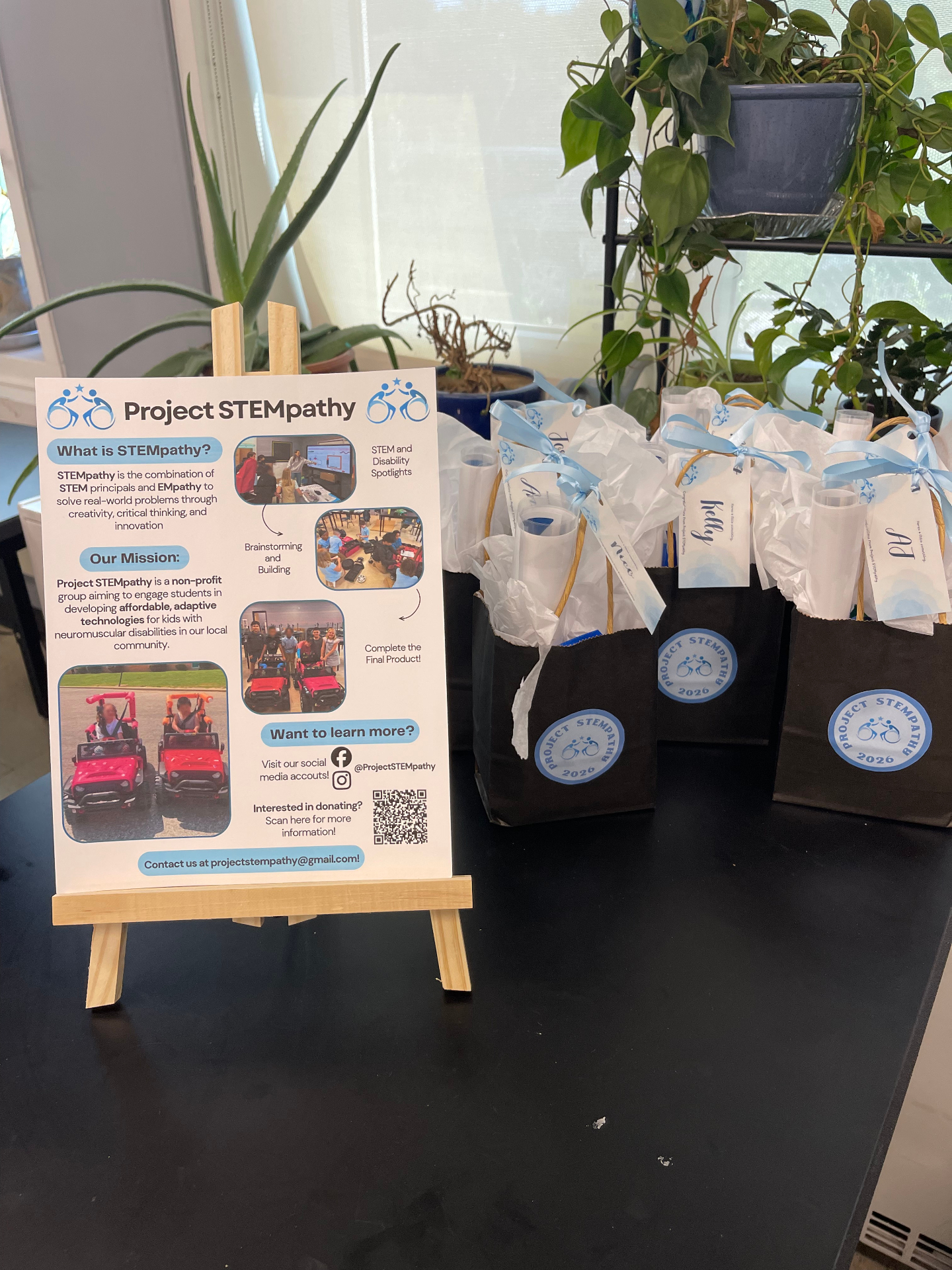 Close-up of a Project STEMpathy display sign beside gift bags at an event table