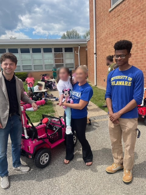 Team members and a family standing beside a finished pink adaptive ride-on car outdoors