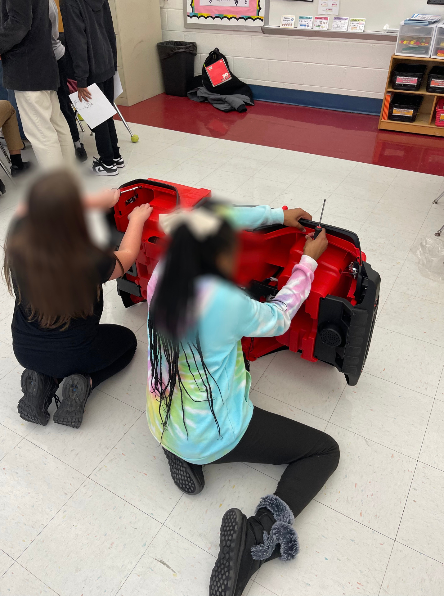 Students using screwdrivers to take apart a red ride-on car during a workshop
