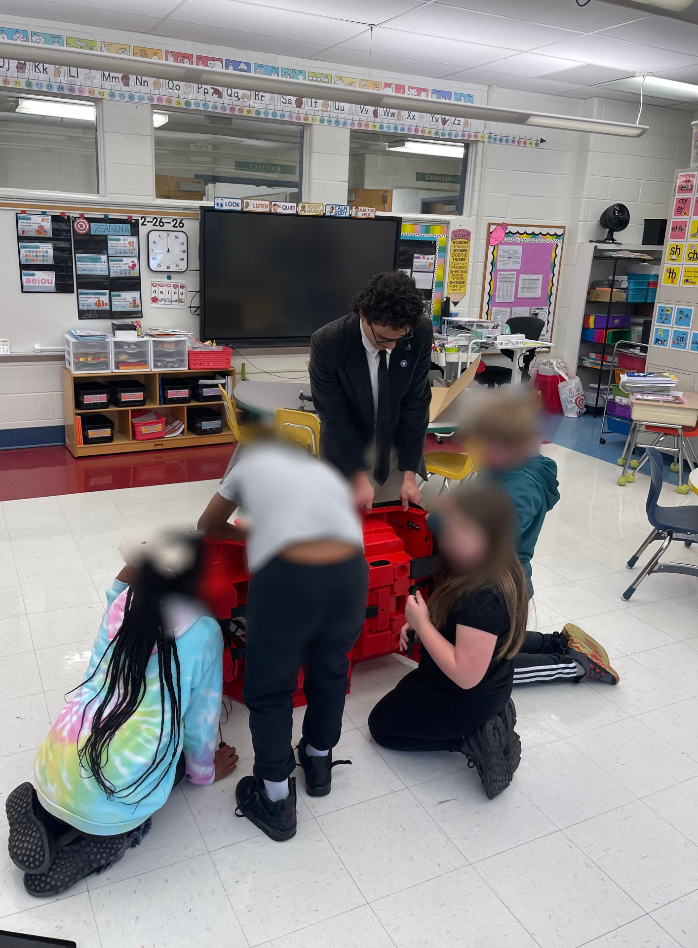 Volunteer guiding students as they work together on an upside-down red ride-on car