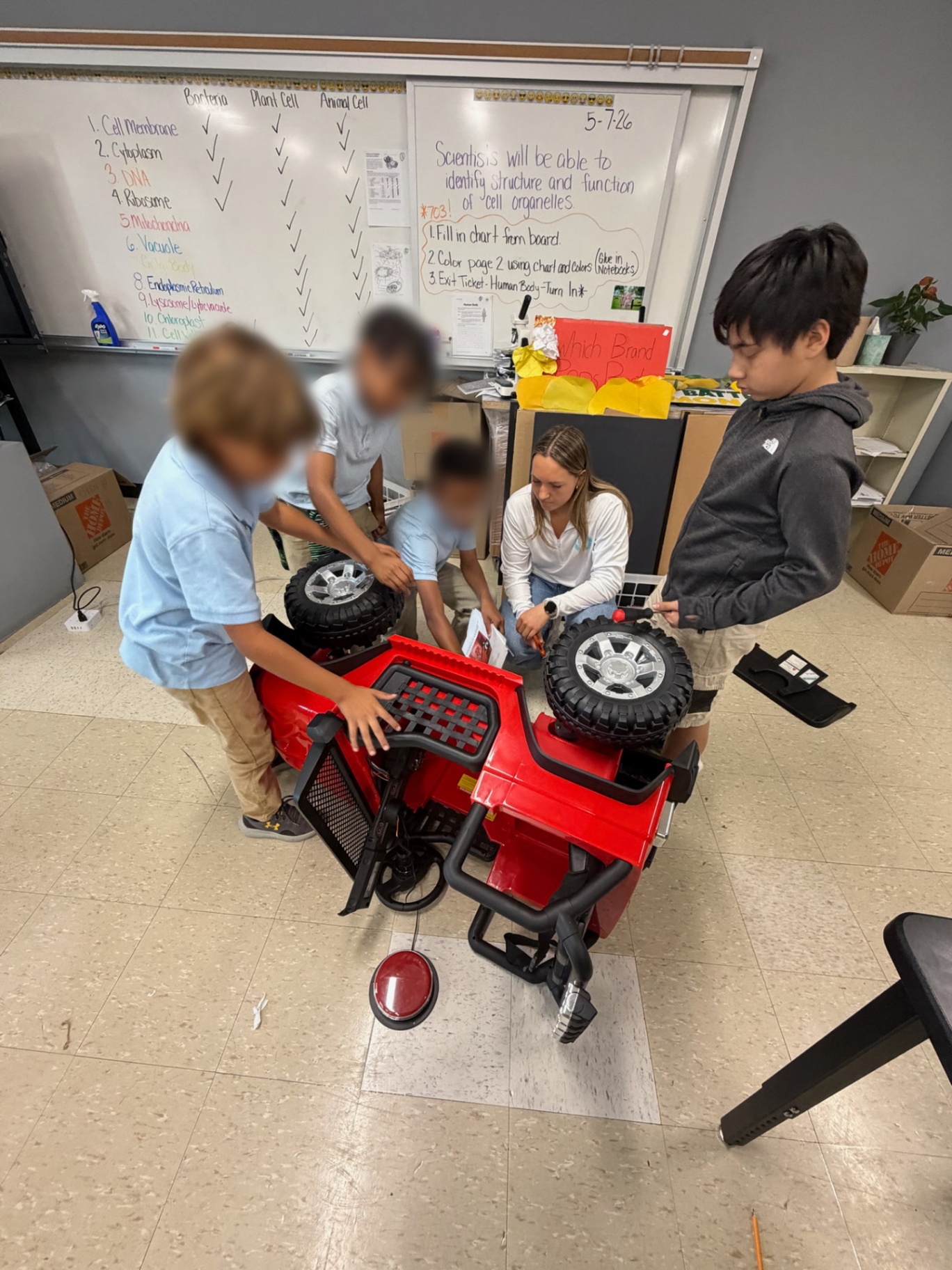 A mentor and students working together on wheels of a red ride-on car
