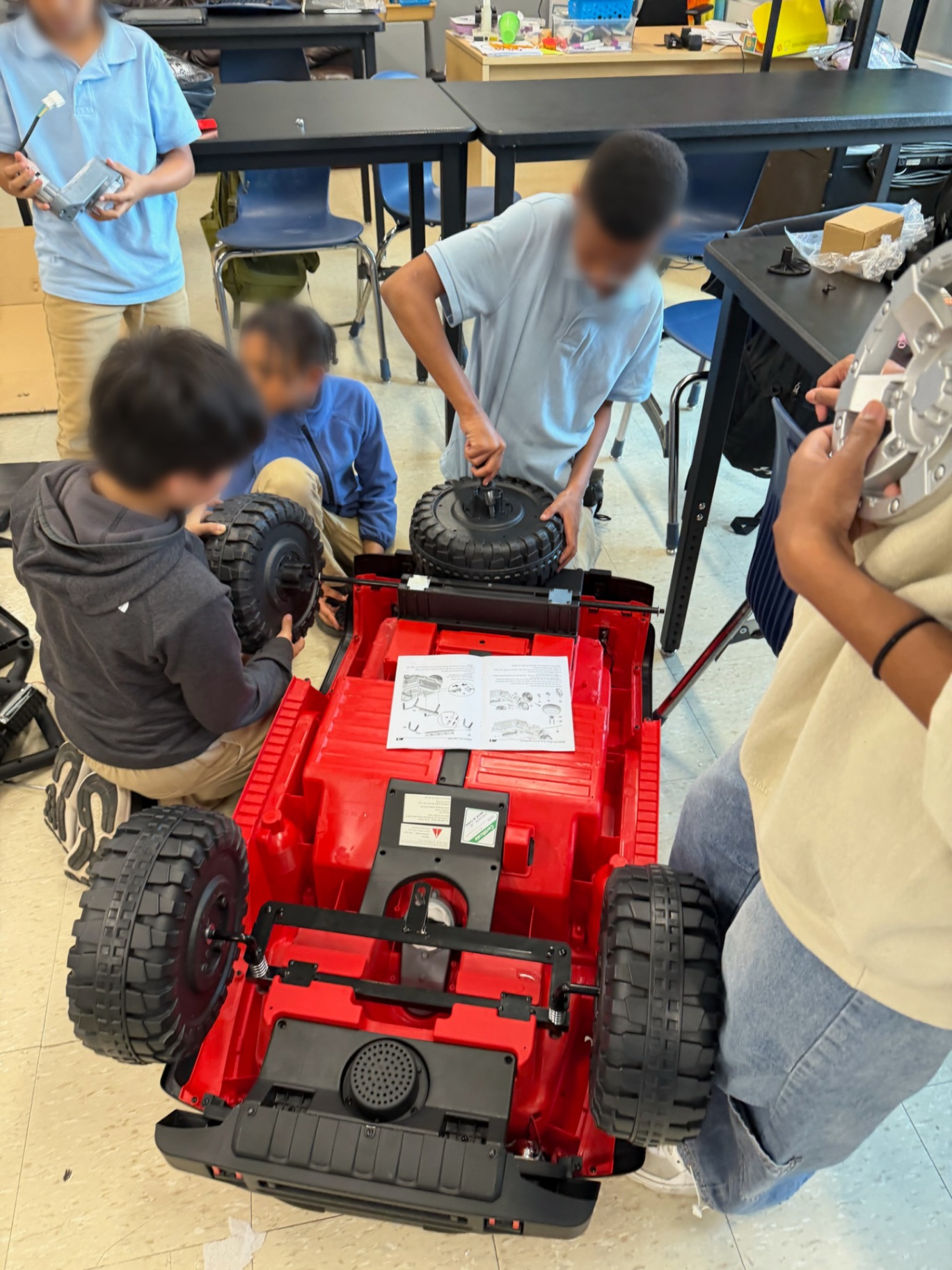 Students installing wheels on the chassis of a red ride-on car