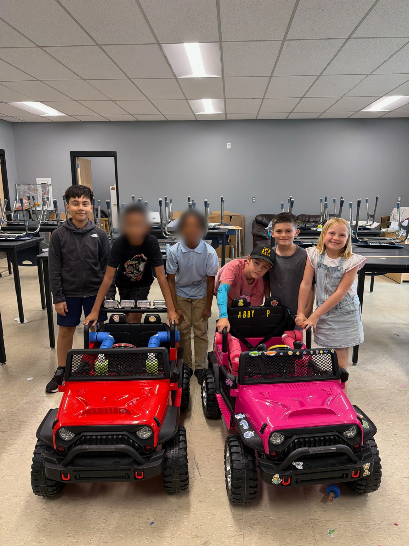 Students posing proudly with two finished adaptive ride-on cars