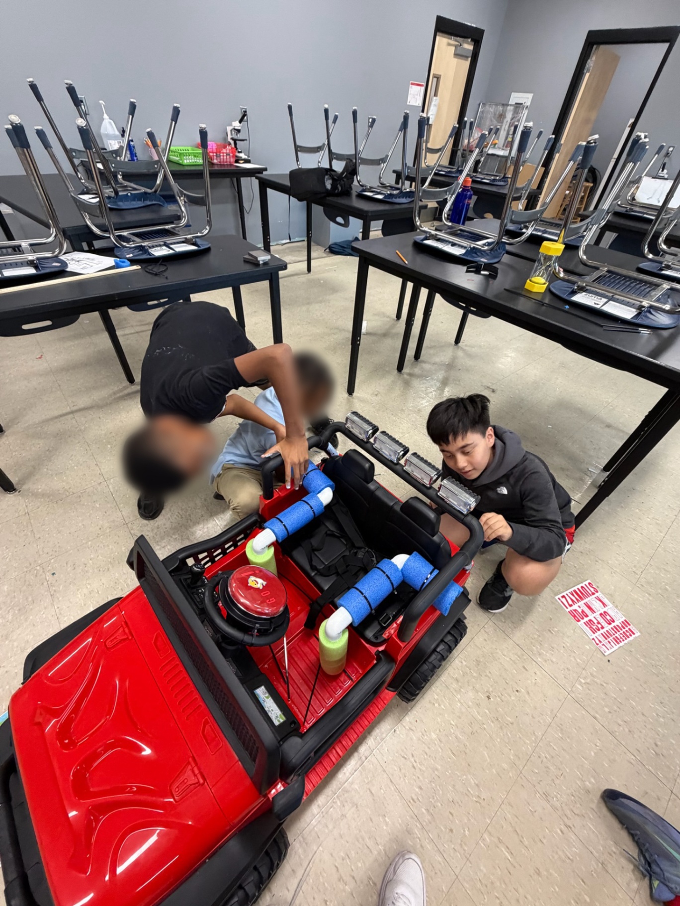 Students assembling the frame of a red adaptive ride-on car